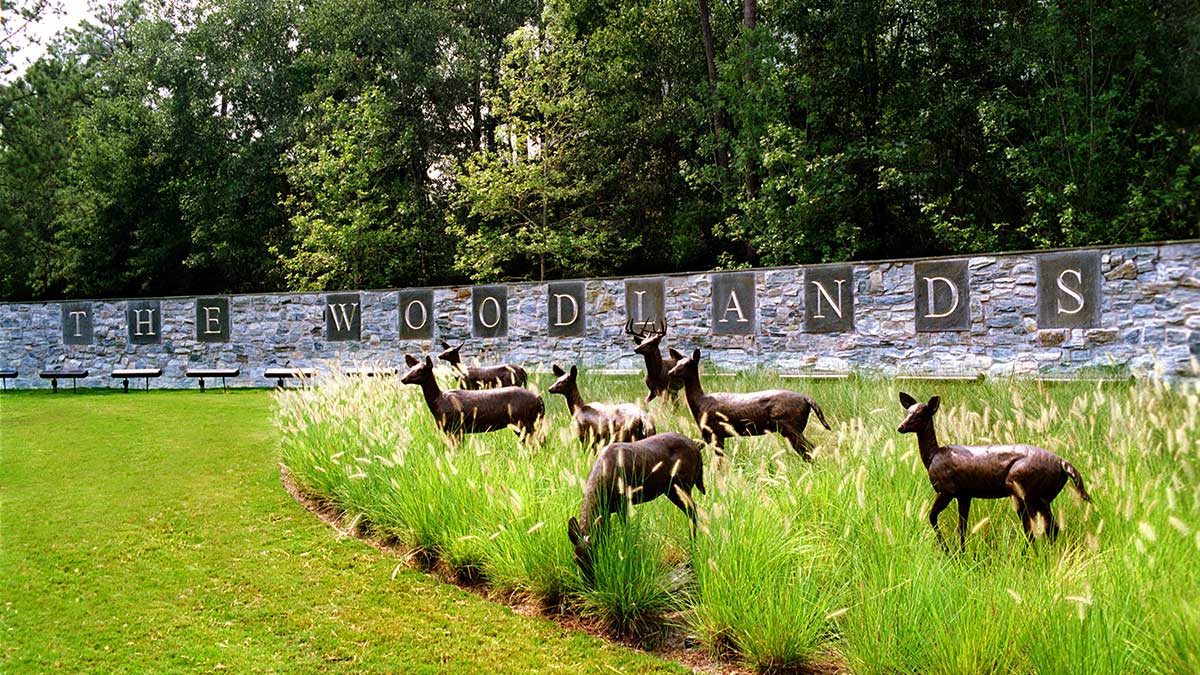 Bronze deer statues in tall grass in front of The Woodlands stone entrance wall